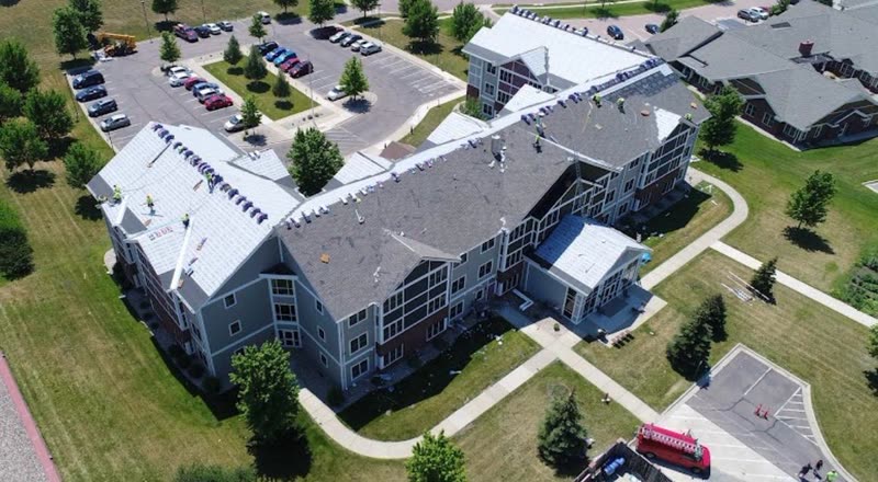 Aerial view of a three-storey apartment building being re-roofed, shingle bundles staged along the ridge