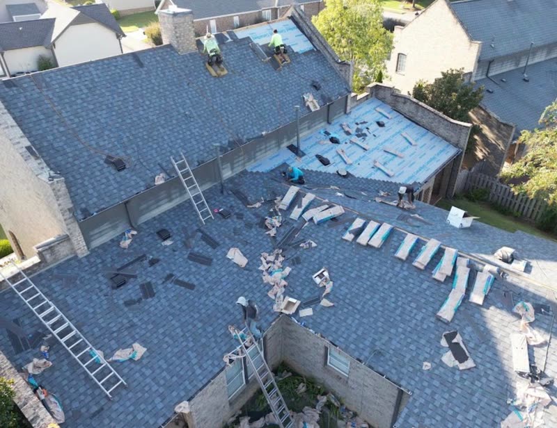 Crews shingling the courtyard roofs of an apartment complex, ladders and materials staged below