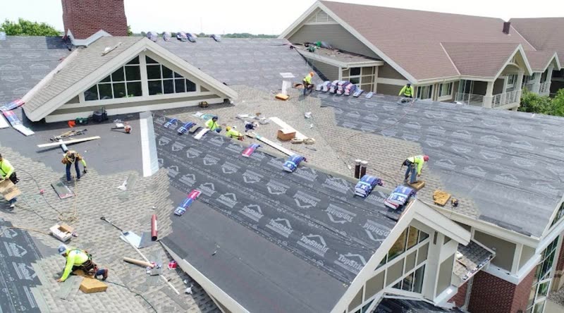 Tear-off in progress on a gabled senior living building, with new underlayment already down