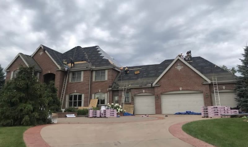 Crew tearing off the roof of a large brick home, ladders up and materials on the drive
