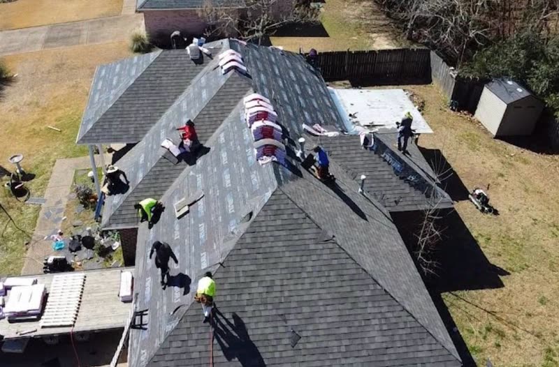 Crew moving shingle bundles across a roof during a full replacement
