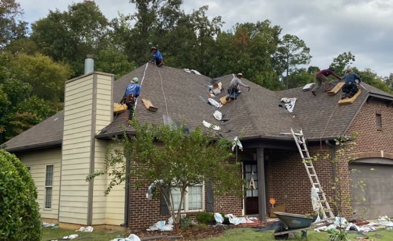Roofing crew working across the hips of a brick and siding home during tear-off
